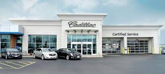 Front view of a white Cadillac car dealership and service center with three luxury cars parked in front.
