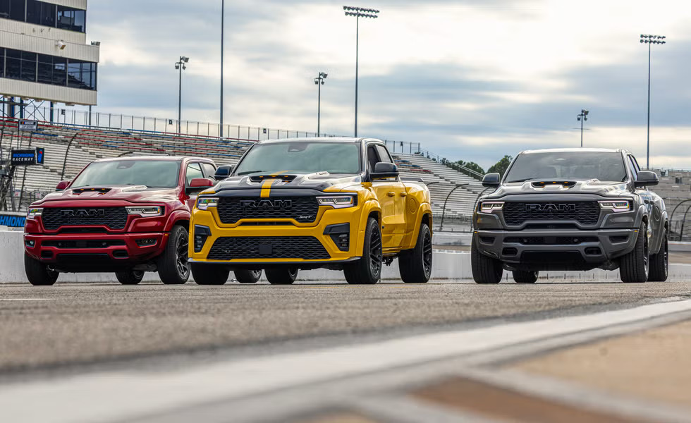 Three modified Ram pickup trucks in red, yellow, and gray parked on a racetrack.