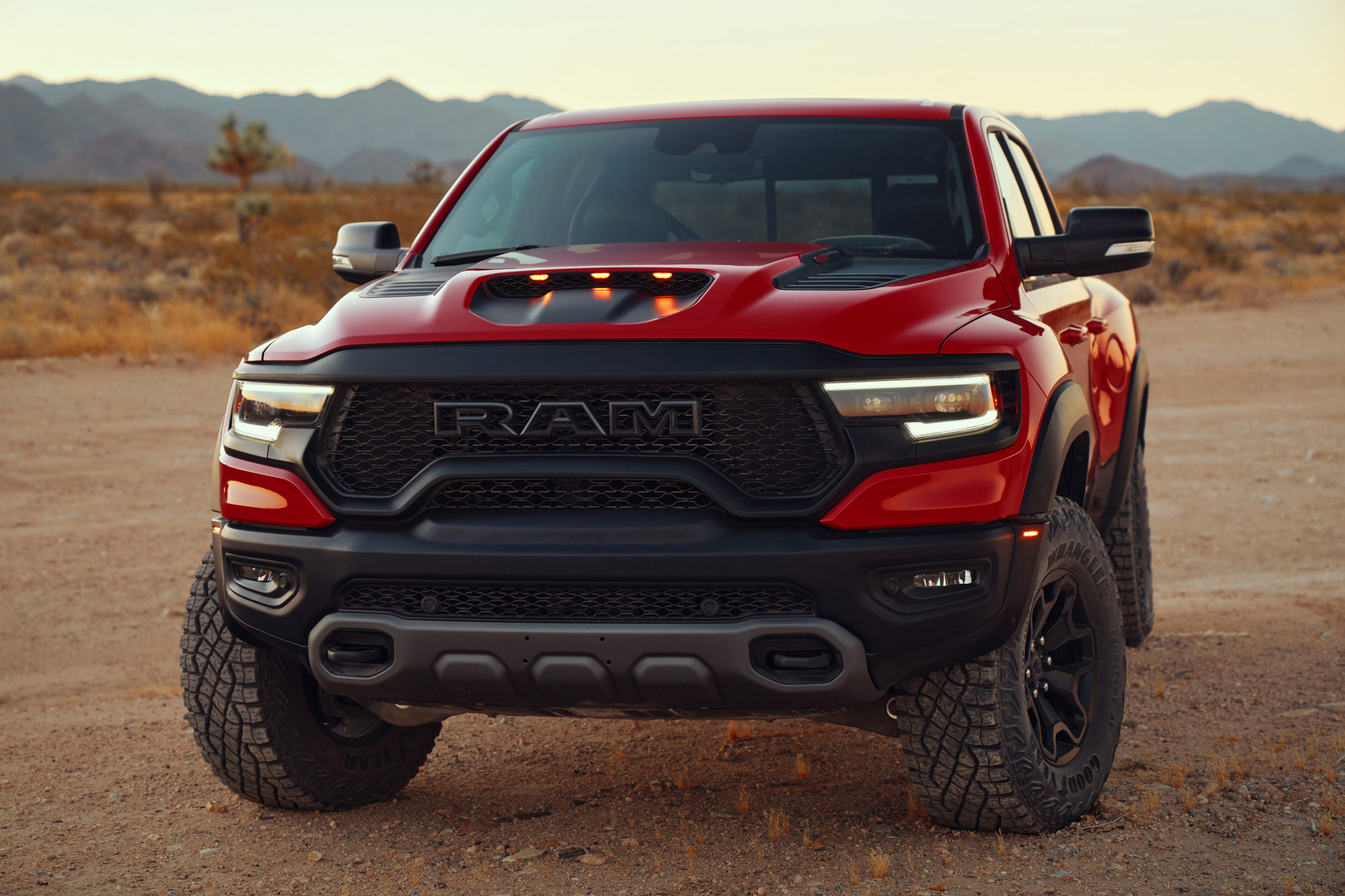 Red Ram 1500 TRX off-road pickup truck parked on a dirt path in a desert landscape at golden hour.