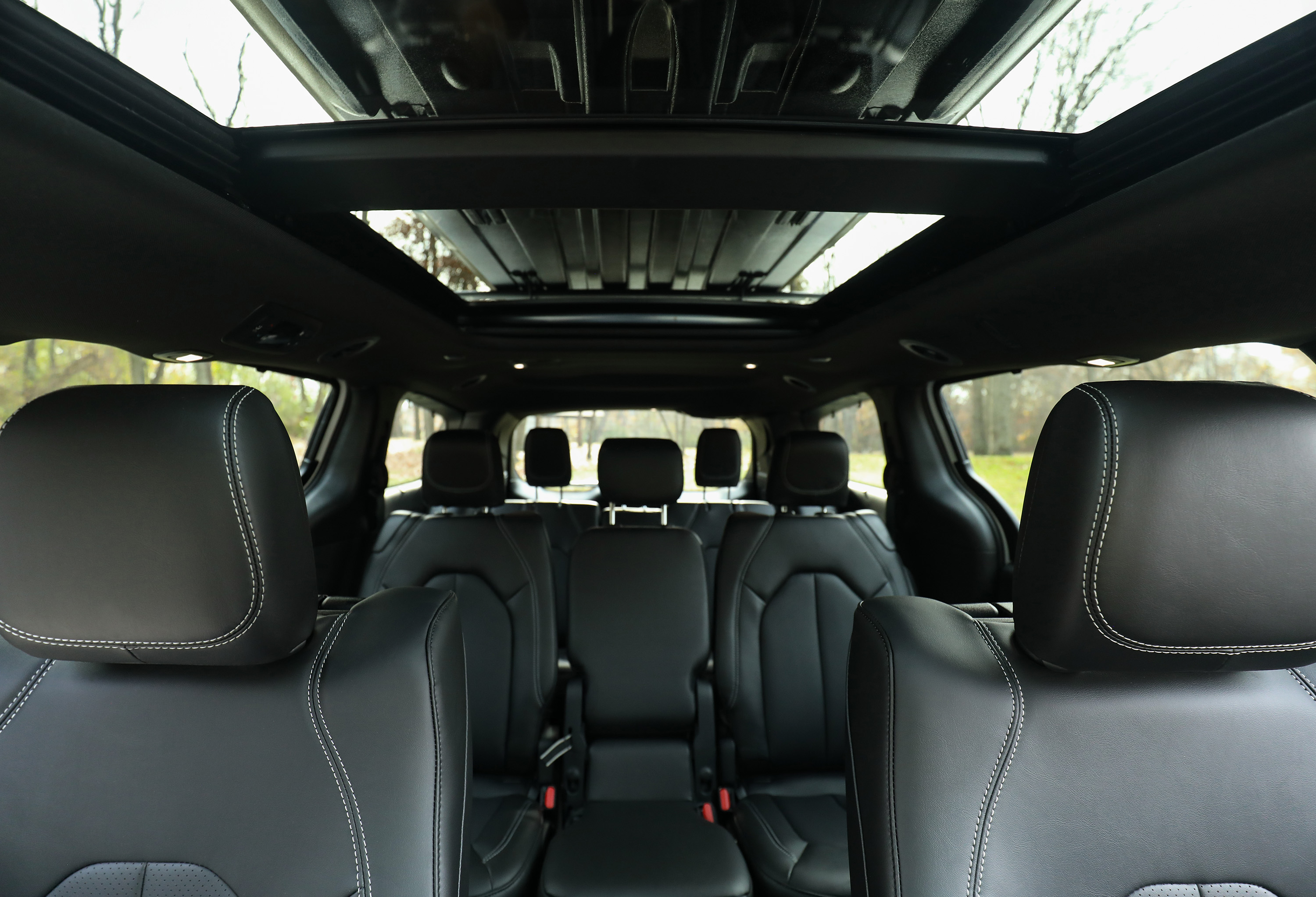 Wide-angle view looking back inside a vehicle featuring black leather three-row seats and a panoramic sunroof.