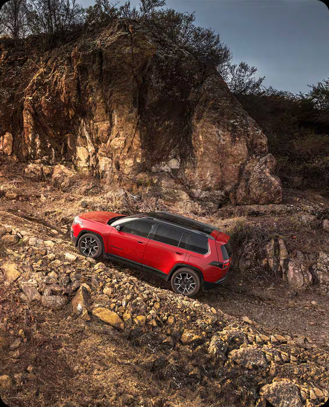 Red SUV navigating a steep, rocky off-road trail beside a large cliff face.