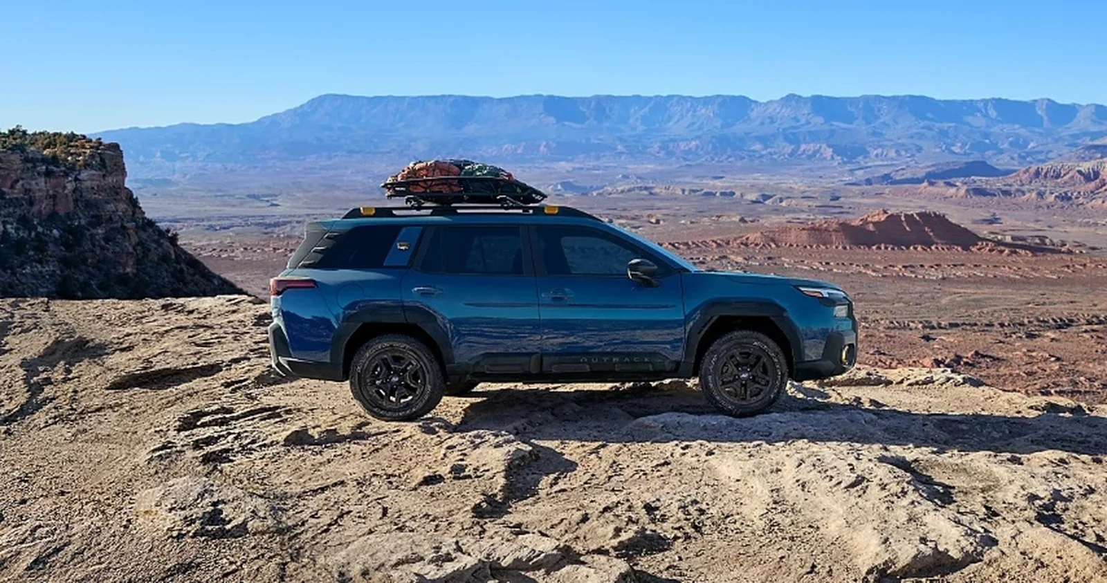 Blue Subaru Outback Wilderness Edition SUV on rocky desert terrain with mountain backdrop.