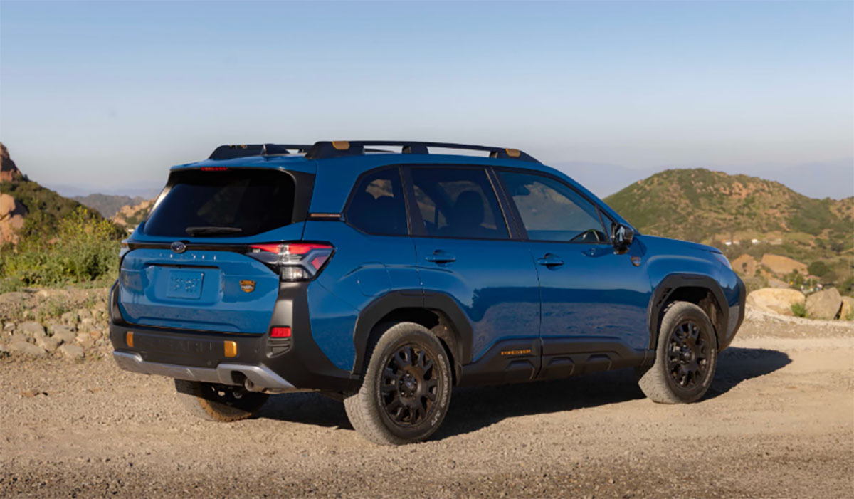 Blue 2027 Subaru Forester Hybrid Wilderness SUV on a dirt road with mountains in the background.