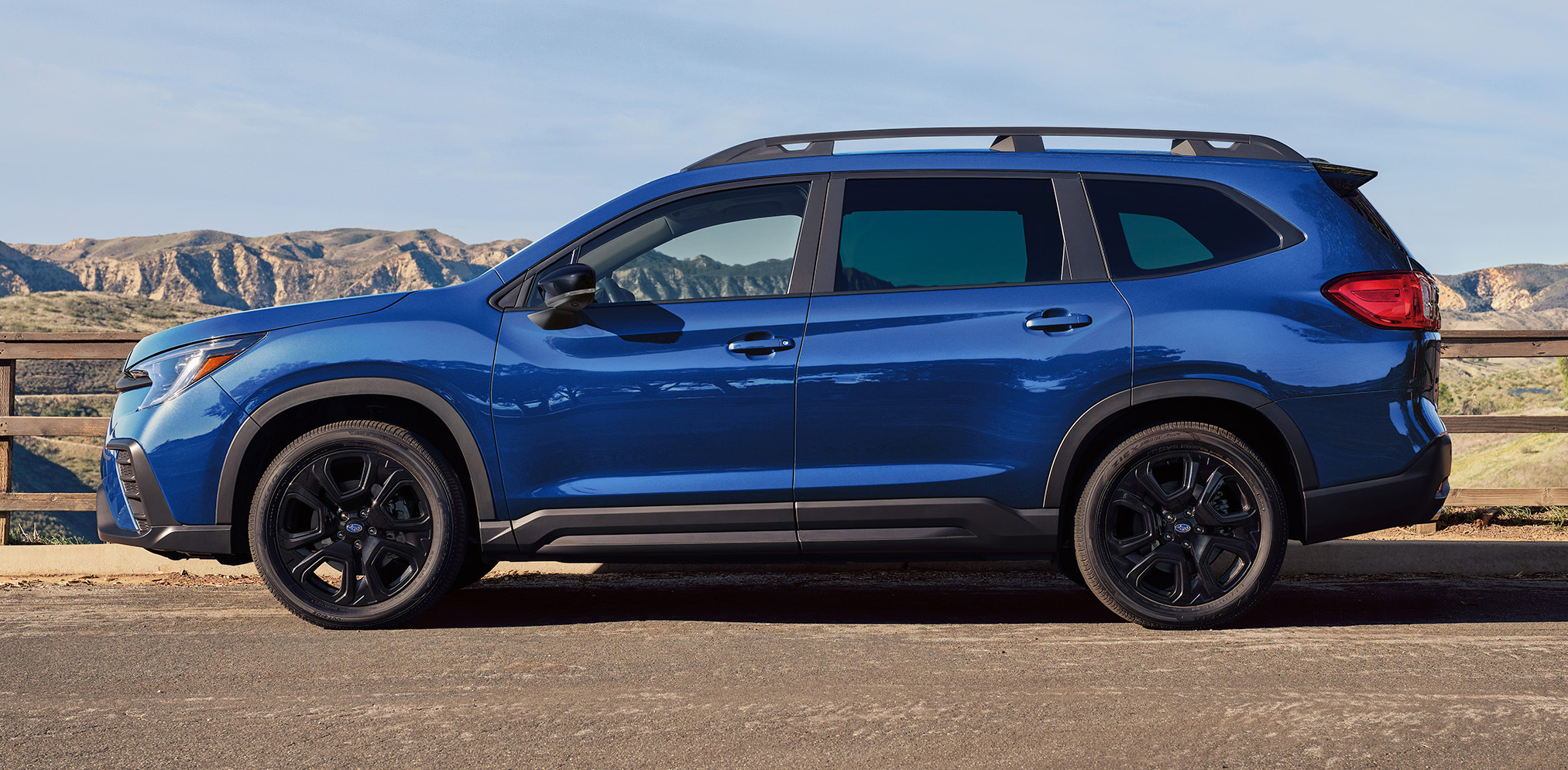 Profile view of a blue 2027 Subaru Ascent parked on an overlook with mountains in the background.