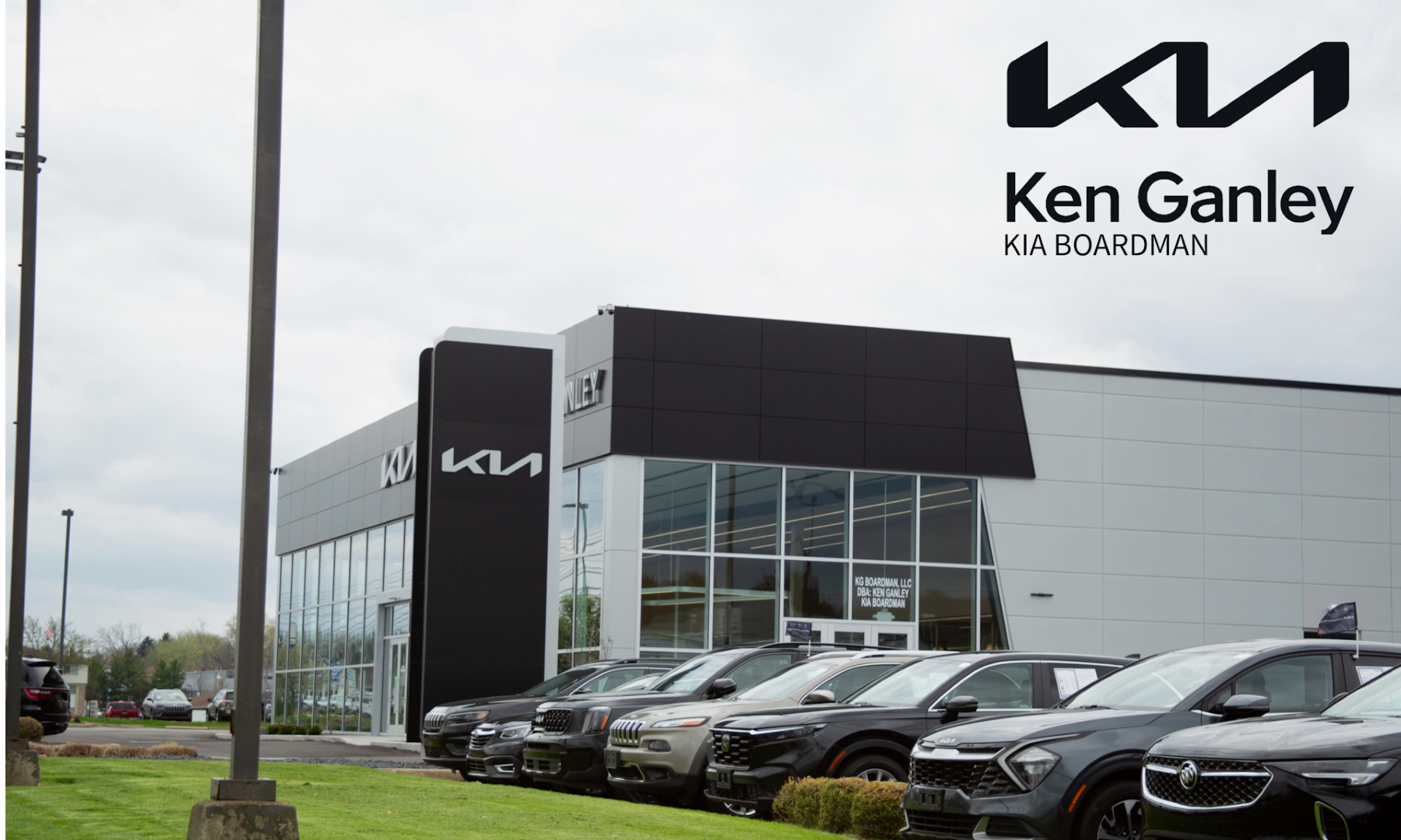 Ken Ganley Kia Boardman dealership exterior with new cars parked in front.