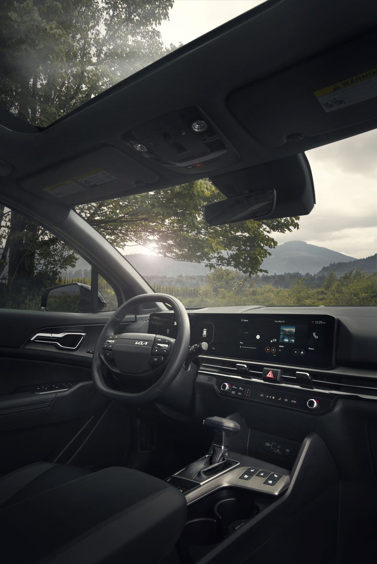 Interior view of a modern Kia car with a large digital display and mountain views through the windshield.
