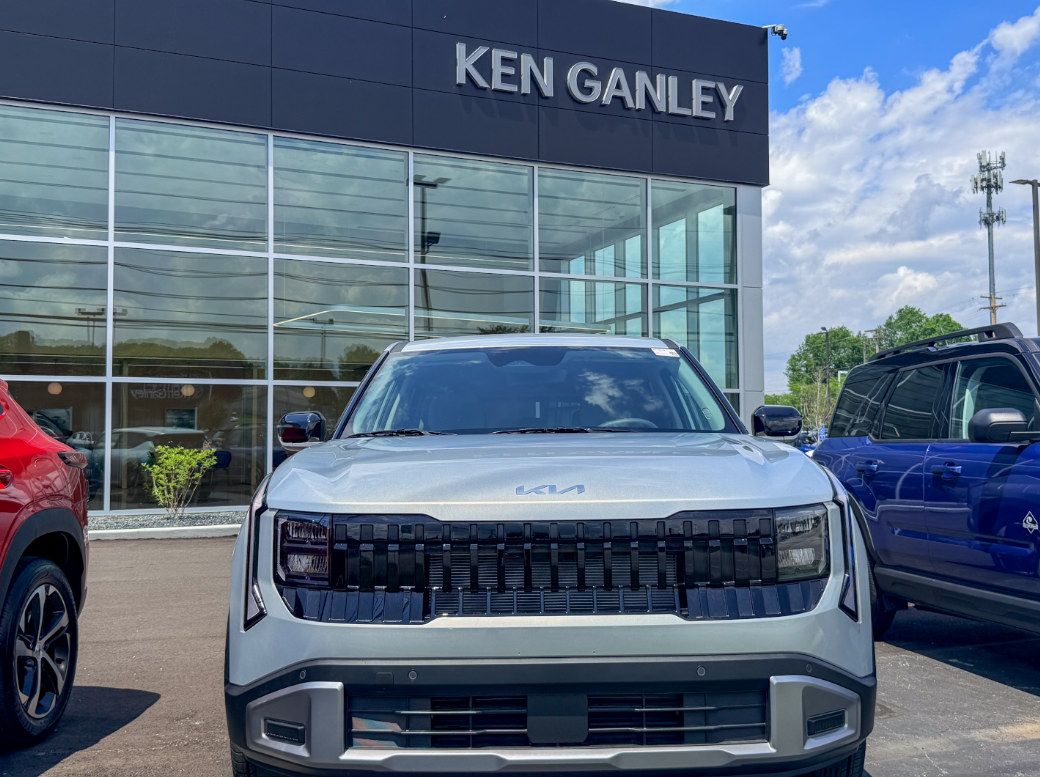Front view of a silver Kia SUV parked outside a Ken Ganley dealership building.