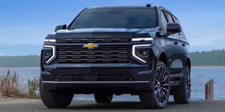 A black Chevrolet SUV parked on a paved road next to a body of water under a clear blue sky.