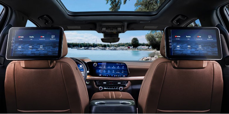 Luxury car interior from the back seat showing dual entertainment screens and a scenic lake view through the windshield.