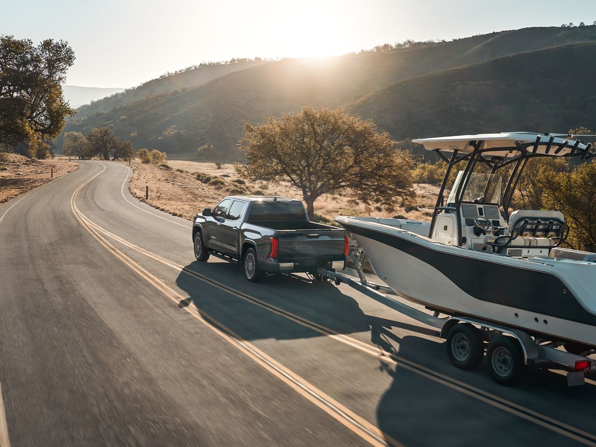A gray Toyota Tundra towing a boat as it drives down the road.