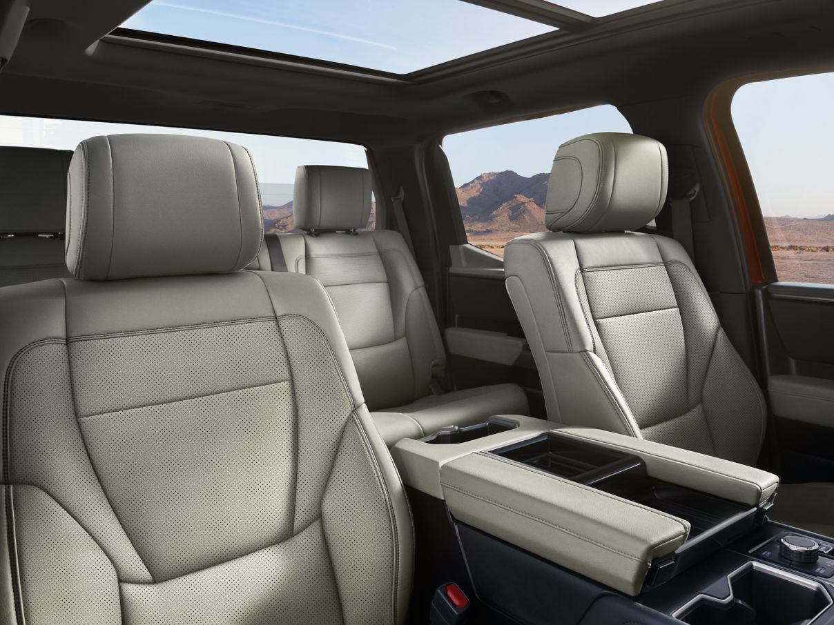 The interior of a Toyota Tundra featuring light beige perforated leather seats, a center console, and a panoramic sunroof.