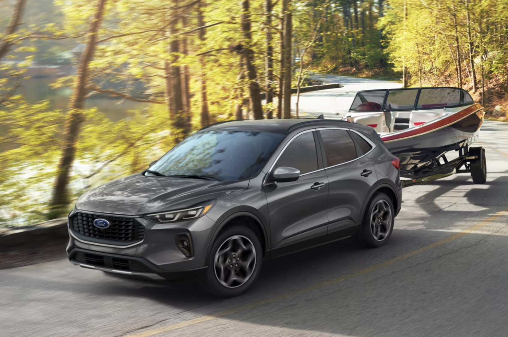 A dark gray Ford Escape SUV towing a speed boat on a trailer down a winding forest road next to a Virginia lake.