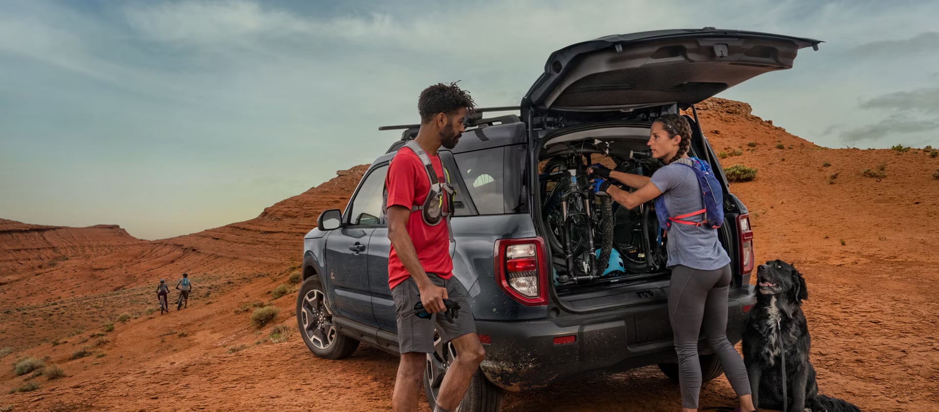 Man and woman loading mountain bikes into the trunk of a blue Ford Bronco Sport in a desert.