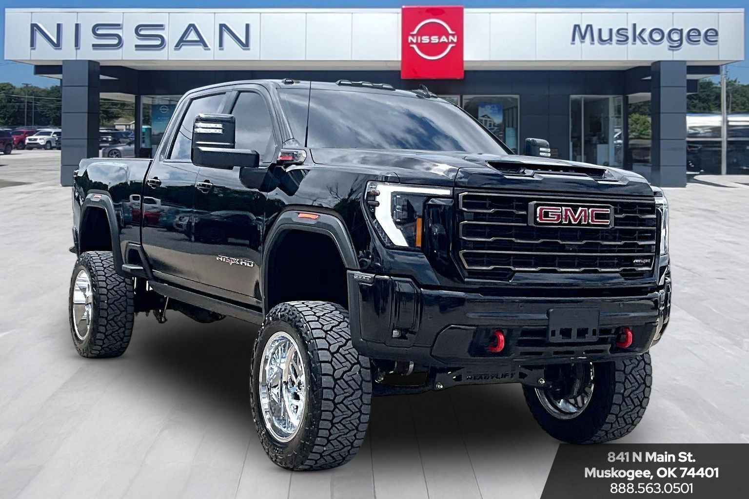 Lifted black GMC Sierra AT4X heavy duty pickup truck with chrome wheels parked at a Nissan dealership.