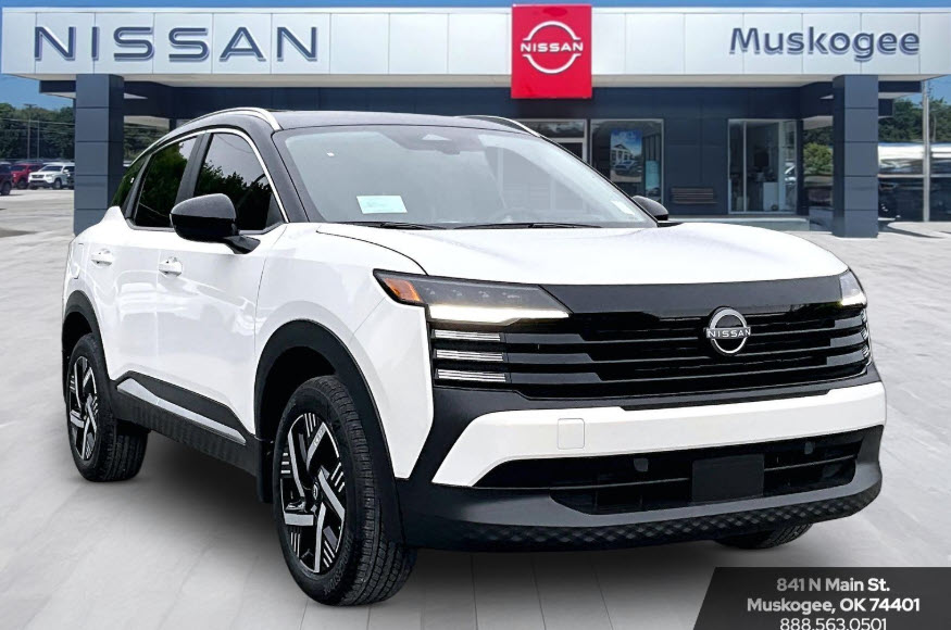 White 2025 Nissan Kicks parked in front of a Nissan Muskogee dealership building.