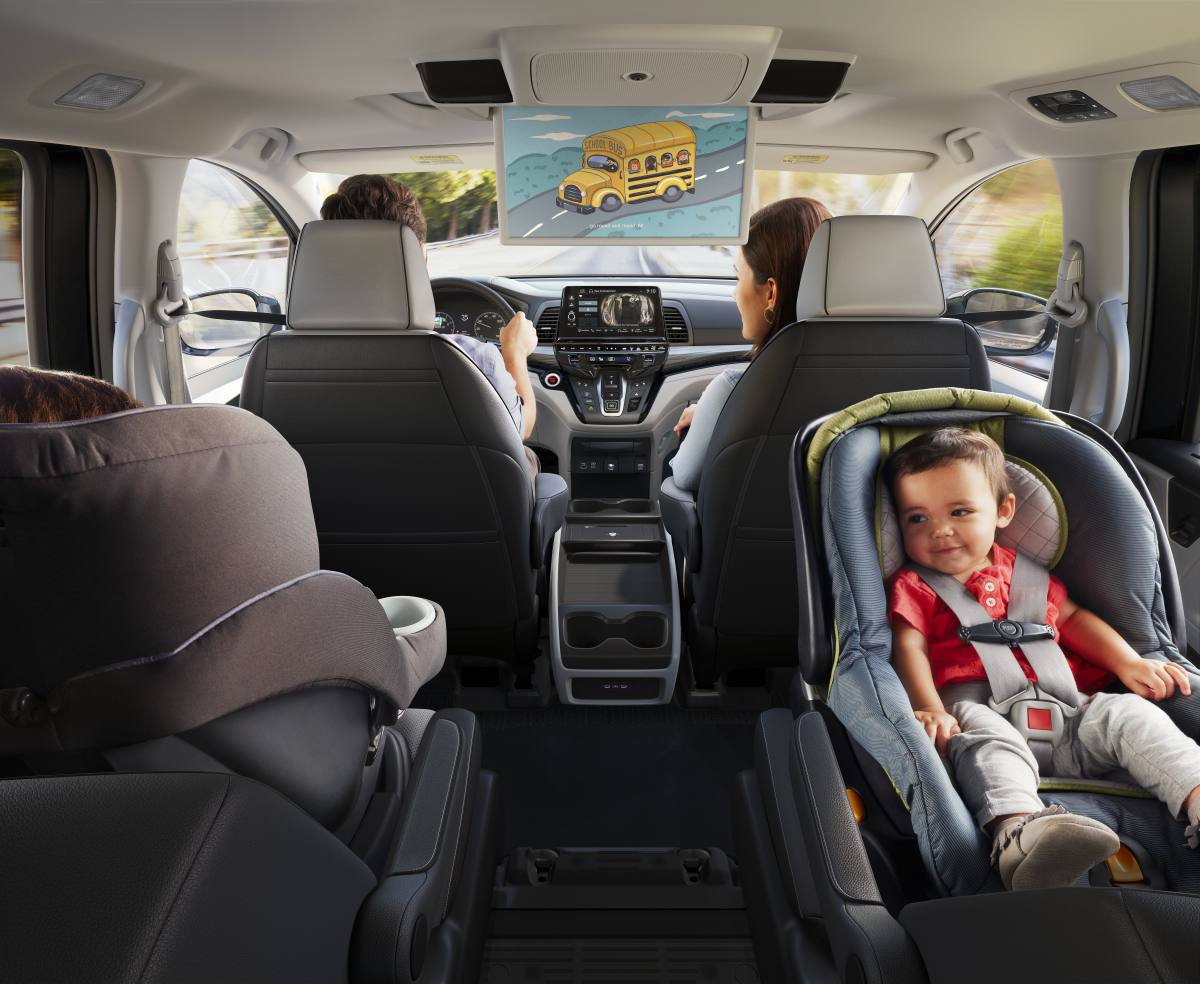 Rear view of car interior with family and child in car seat watching movie.