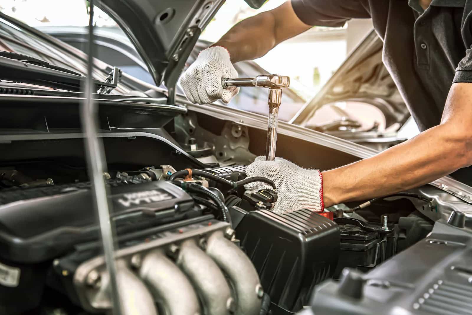 Mechanic working on car engine with socket wrench, wearing gloves.