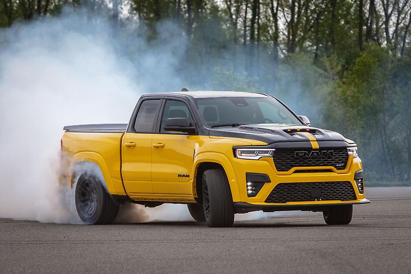 Yellow and black Ram truck performing a burnout on pavement with thick white tire smoke.