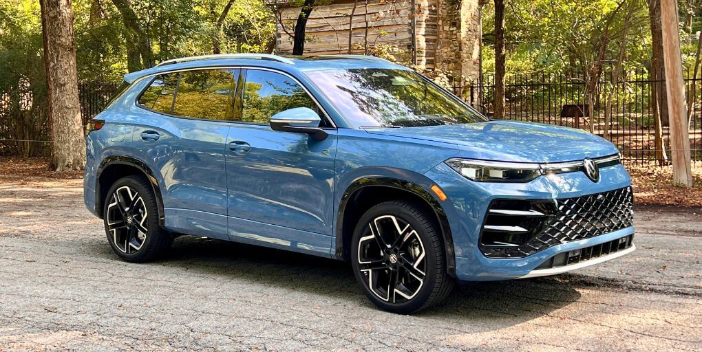 Blue Volkswagen Taos SUV on asphalt driveway with tree background.