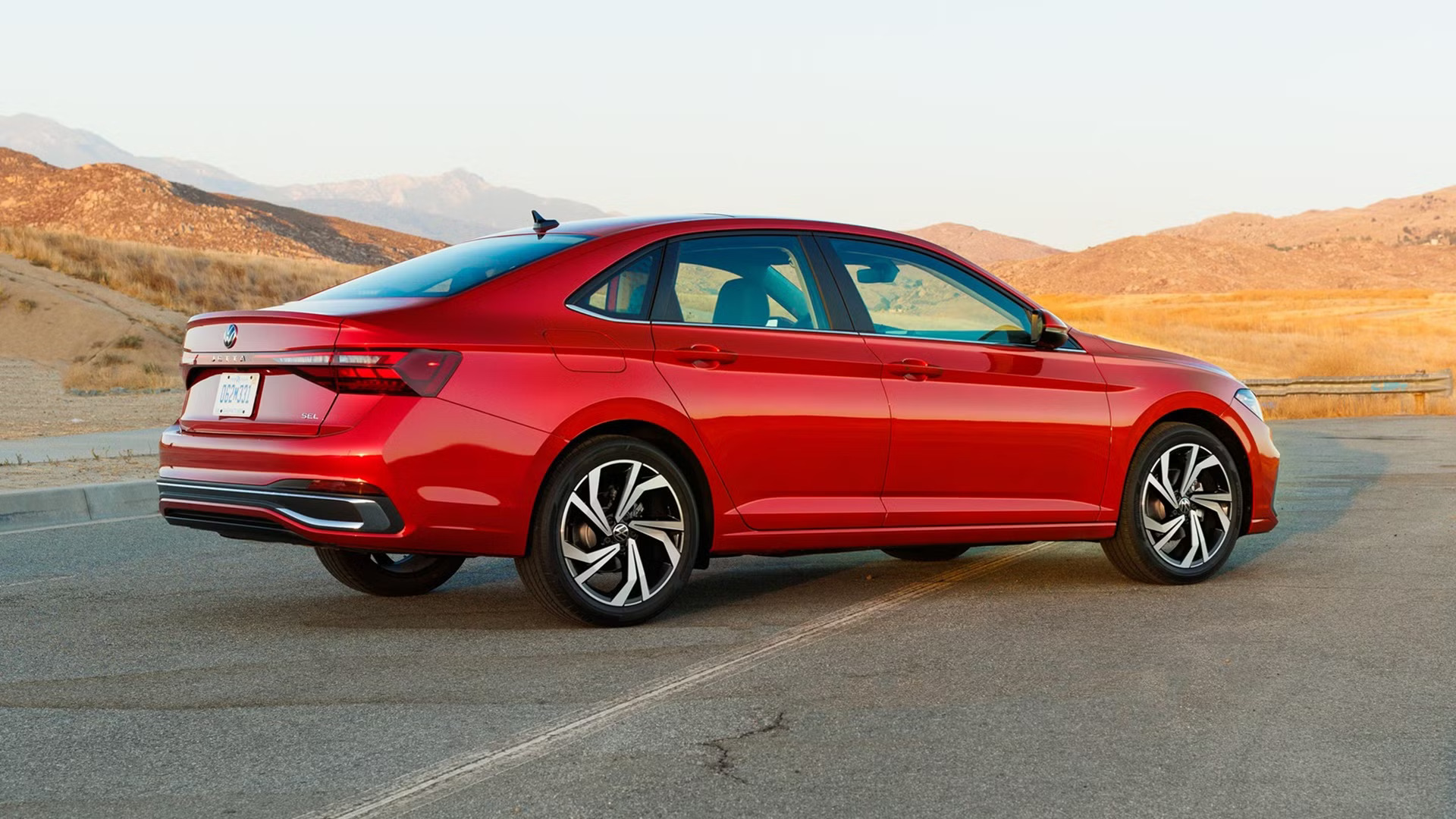 Red Volkswagen Virtus sedan parked on asphalt road with mountain backdrop.