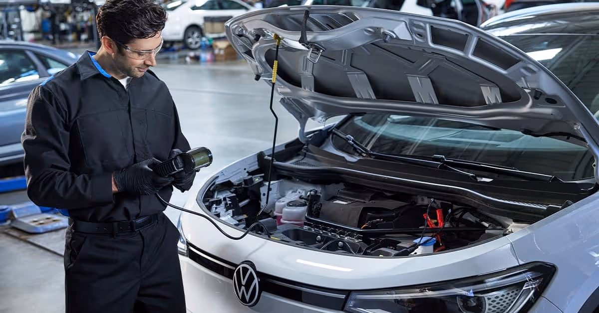 Mechanic inspecting under the hood of a white Volkswagen ID.4 electric vehicle.