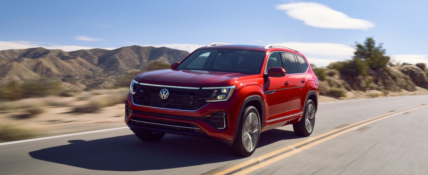 Red Volkswagen Atlas SUV driving on a highway with mountains in the background.