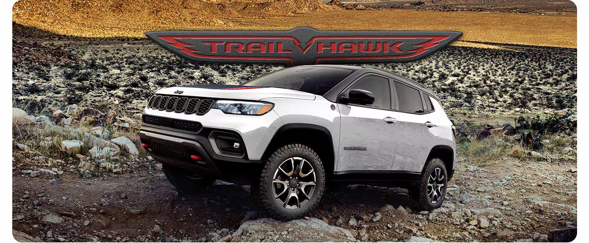 White Jeep Compass Trailhawk parked on a rocky desert trail with Trailhawk logo above it.