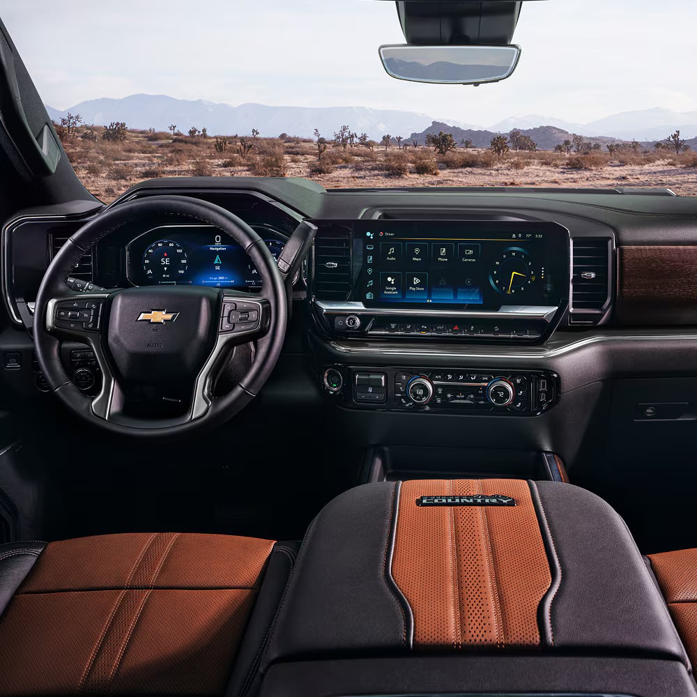Modern interior dashboard of a Chevrolet High Country vehicle showing the steering wheel, screens, and desert view.