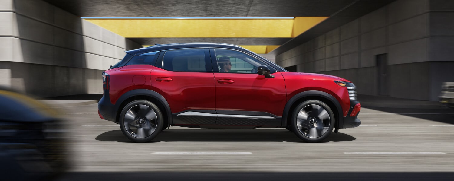 Red two-tone 2027 Nissan Kicks driving under a concrete urban overpass with yellow accents.