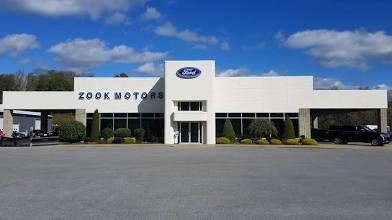 Zook Motors Ford dealership building under a bright blue sky with white clouds.