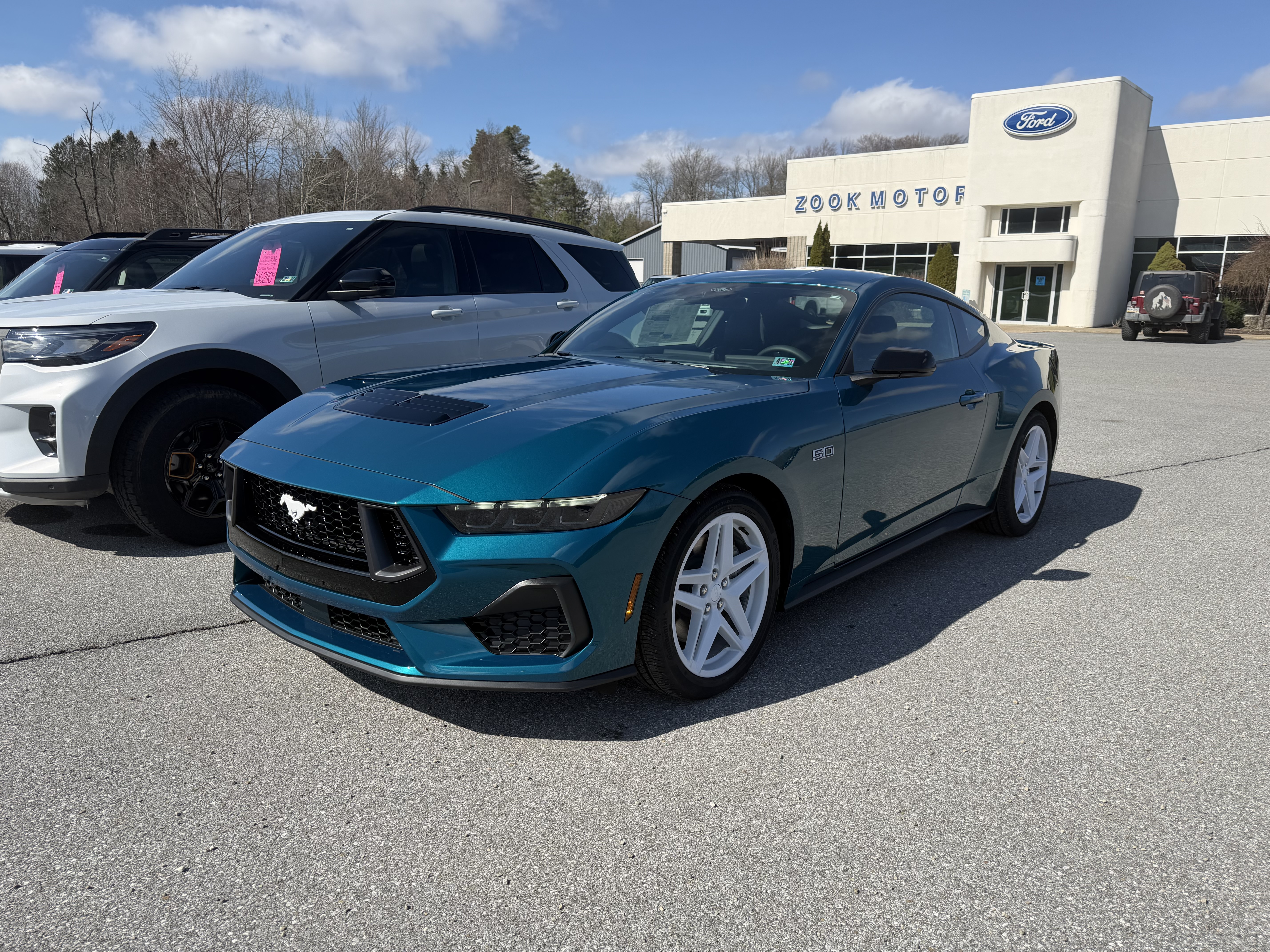 Teal Ford Mustang GT with white wheels parked at a Zook Motors dealership.