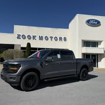 A gray Ford F-150 pickup truck parked in front of Zook Motors dealership.