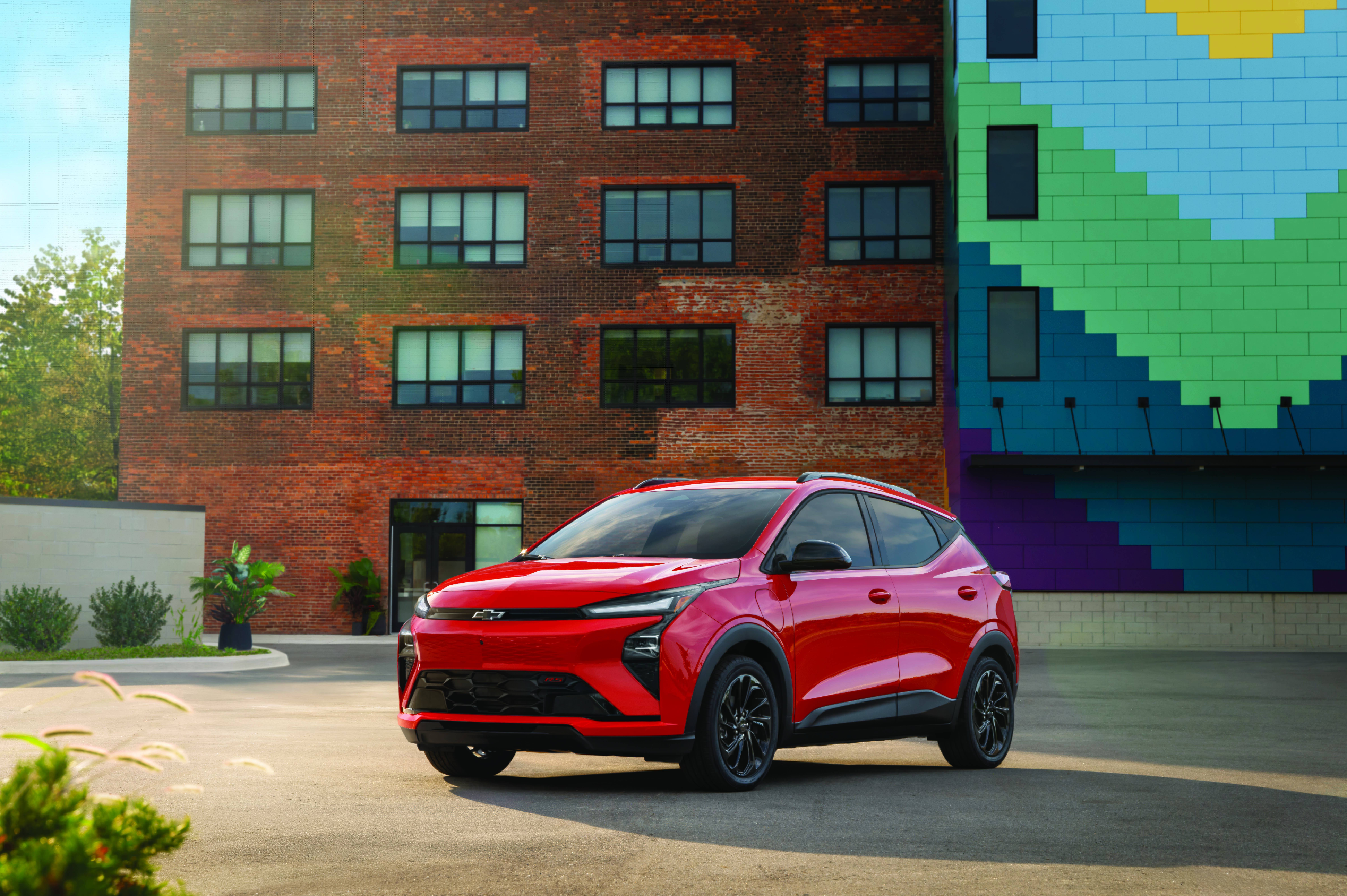 A red Chevrolet Bolt EUV parked in an urban courtyard with a brick building and colorful mural.