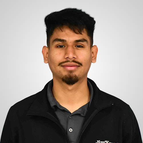 A young man with dark hair and a goatee wearing a black jacket against a grey background.