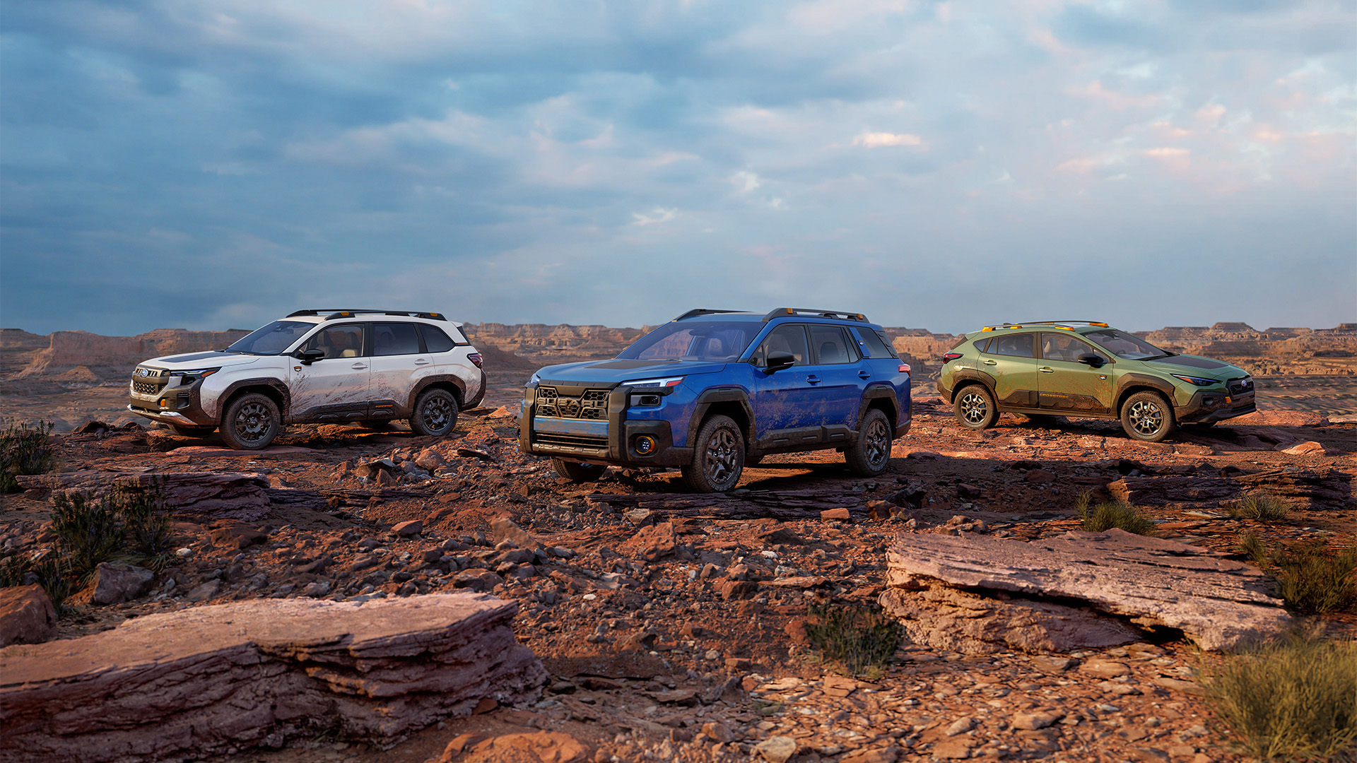 Three mud-splattered Subaru Wilderness SUVs parked on a rocky desert plateau under a cloudy sky.