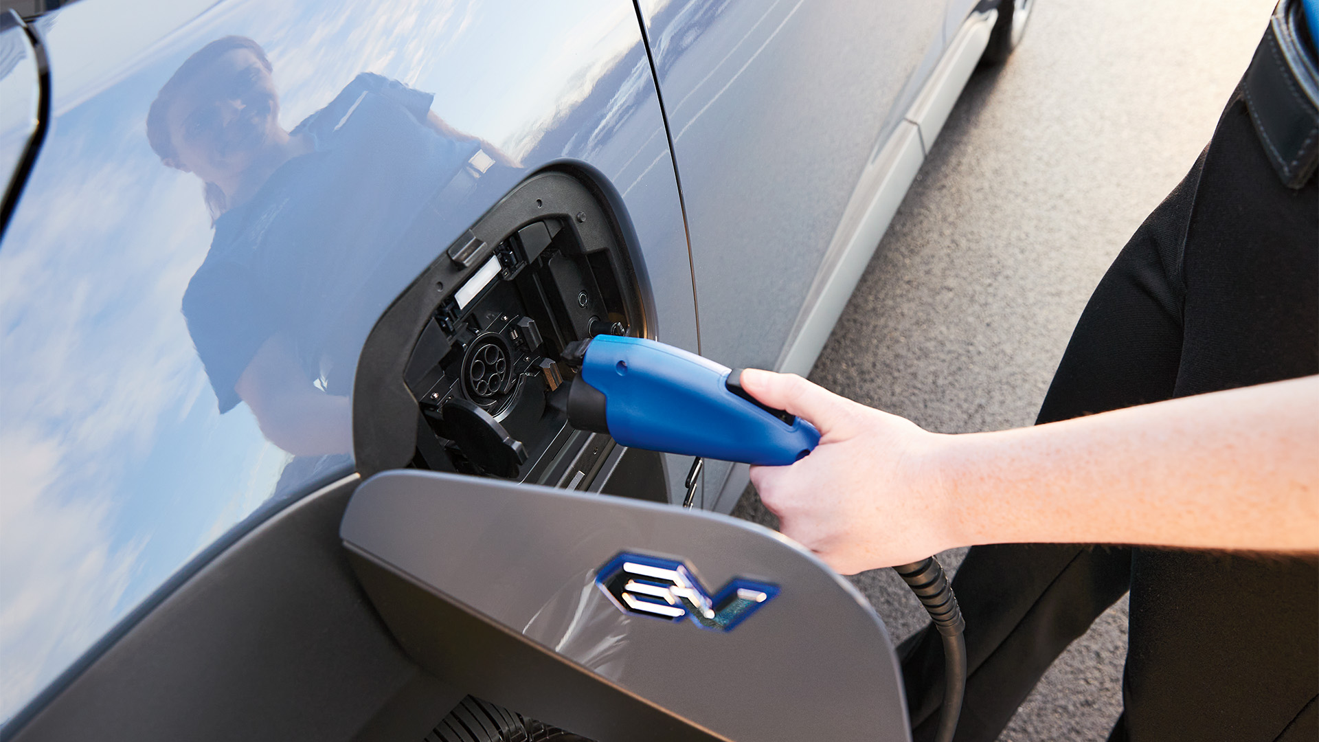 A person plugging a blue electric vehicle charger into a gray car's charging port.