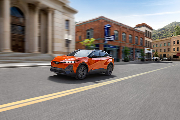An orange electric SUV driving down a city street with motion blur.