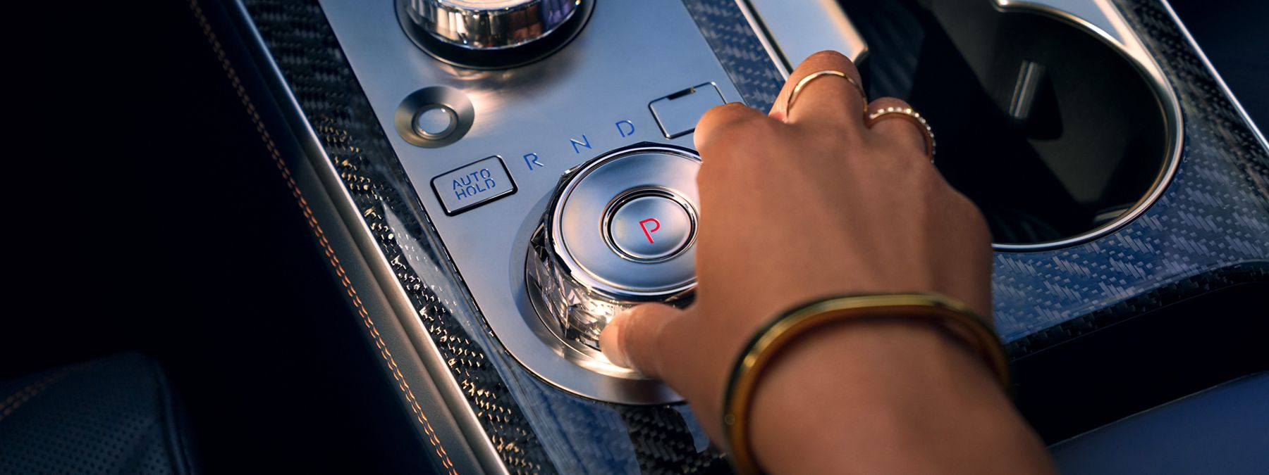 A person's hand turning a crystal rotary gear shift dial in a Genesis luxury SUV interior.