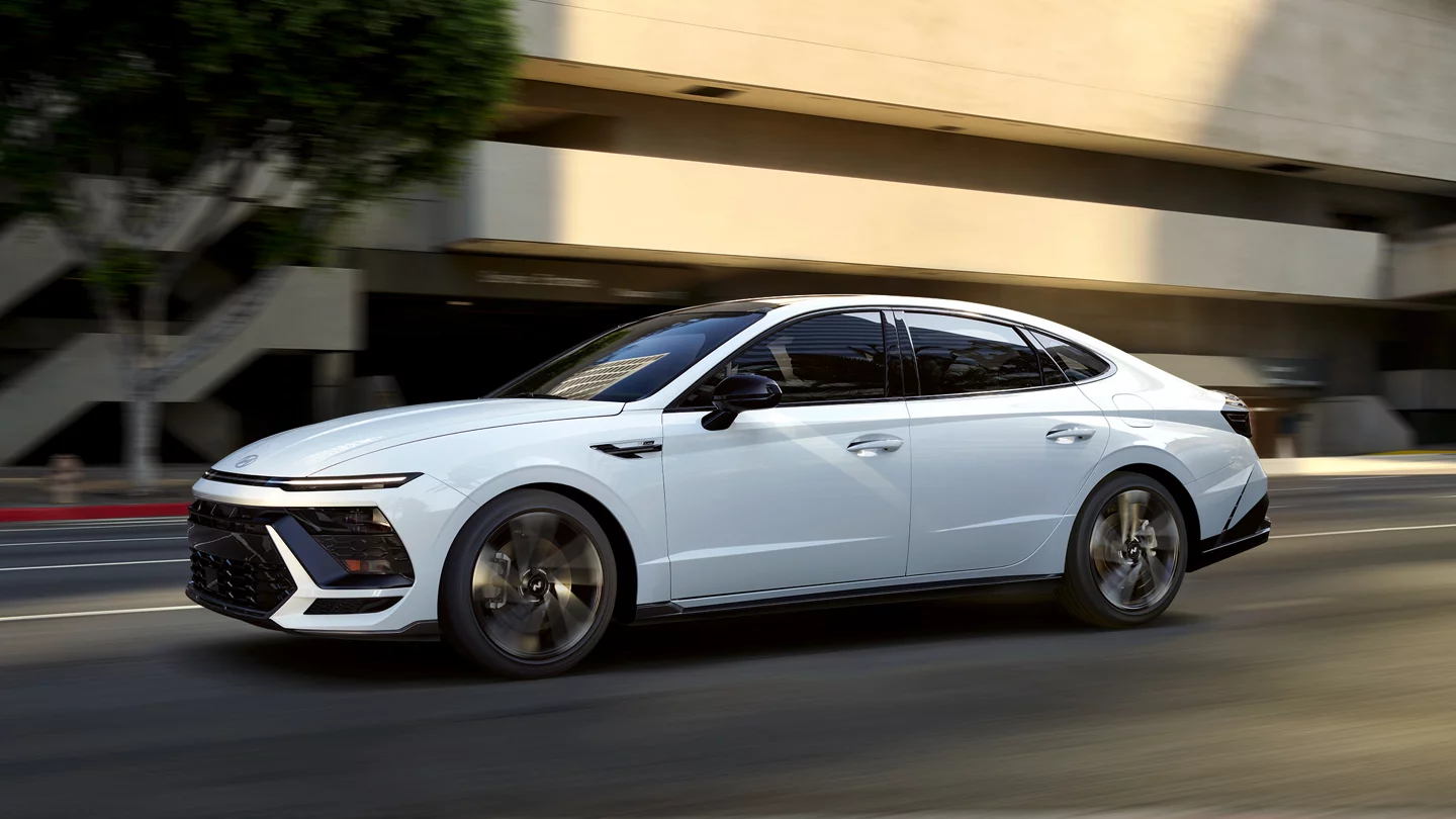A white Hyundai Sonata N Line driving on a city street at sunset.
