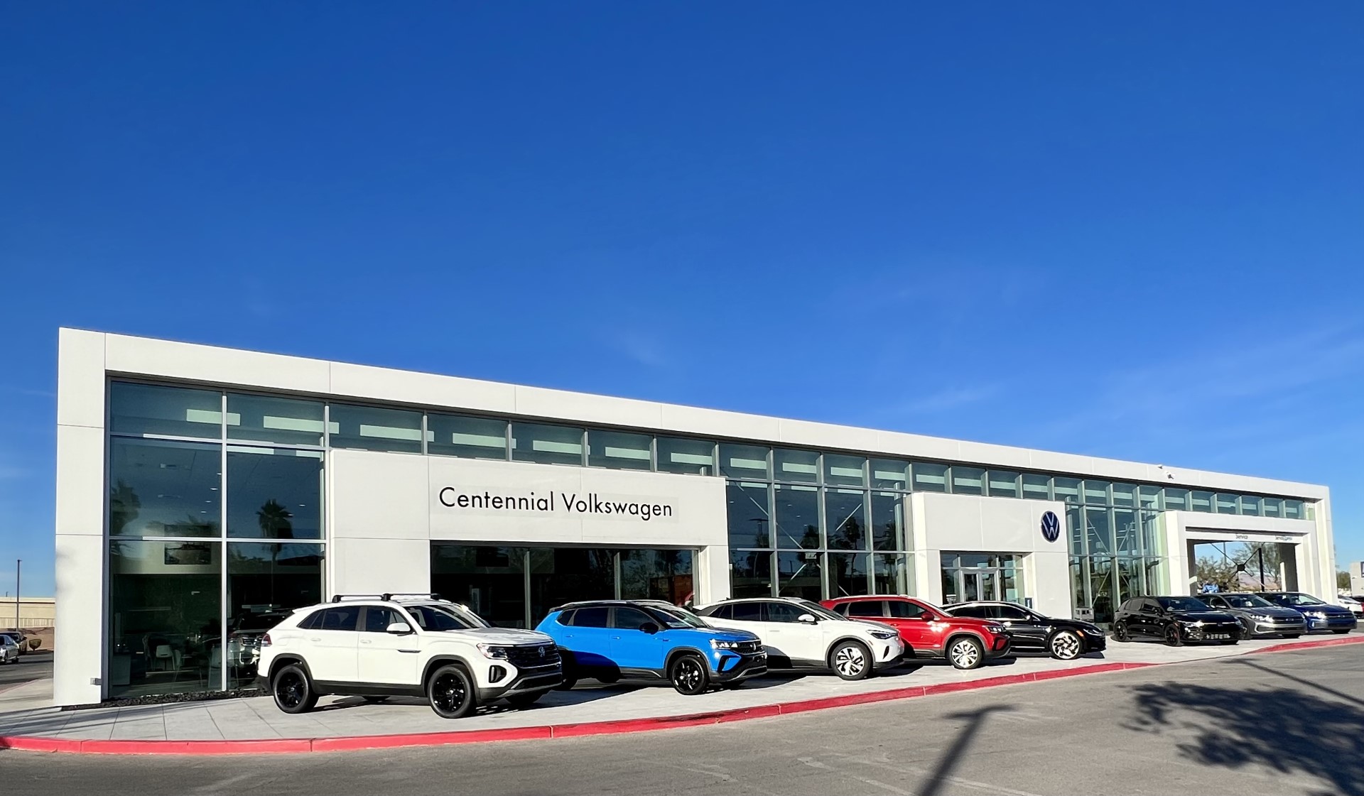 Centennial Volkswagen dealership with new cars parked outside, under sunny blue sky.