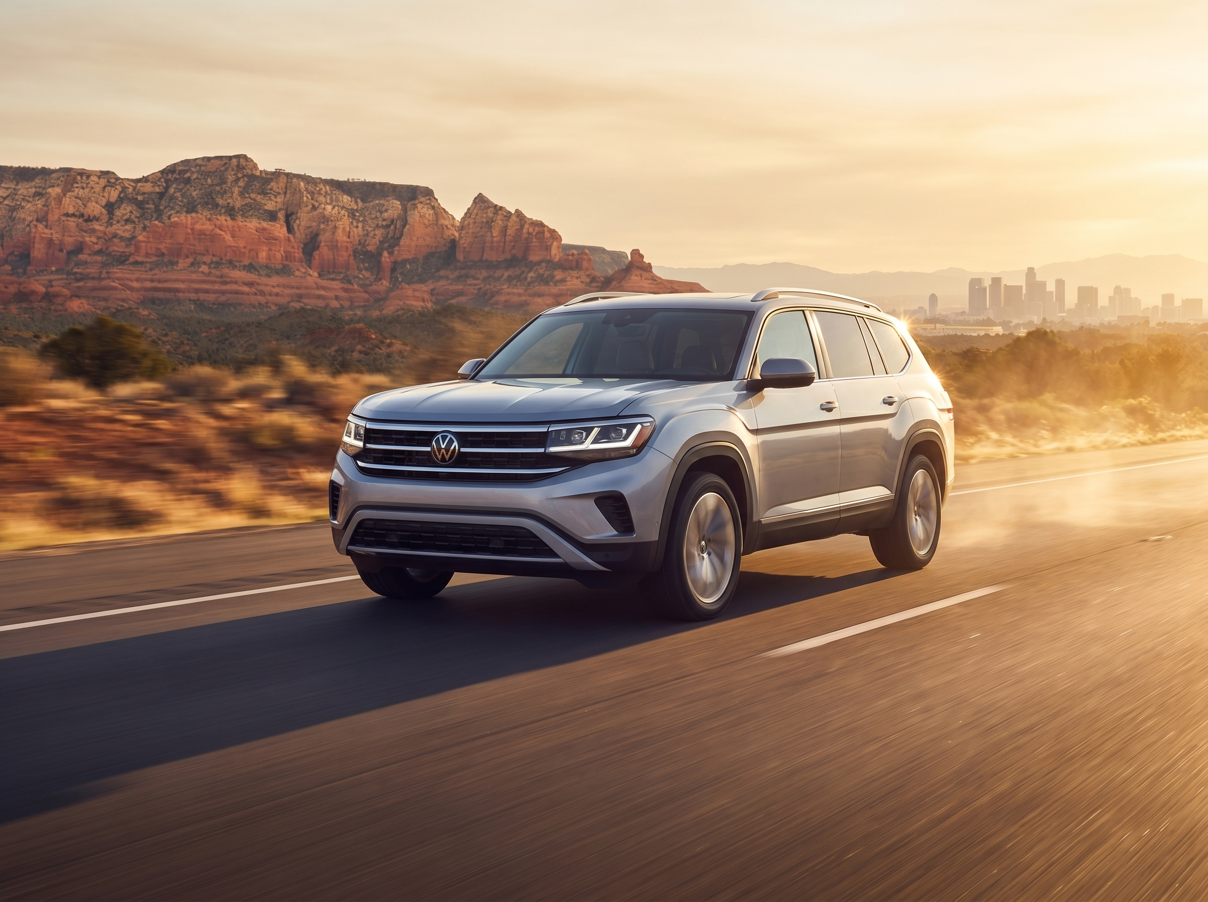 Silver Volkswagen Atlas SUV driving on a highway through a desert landscape at sunset with a city skyline in the distance.