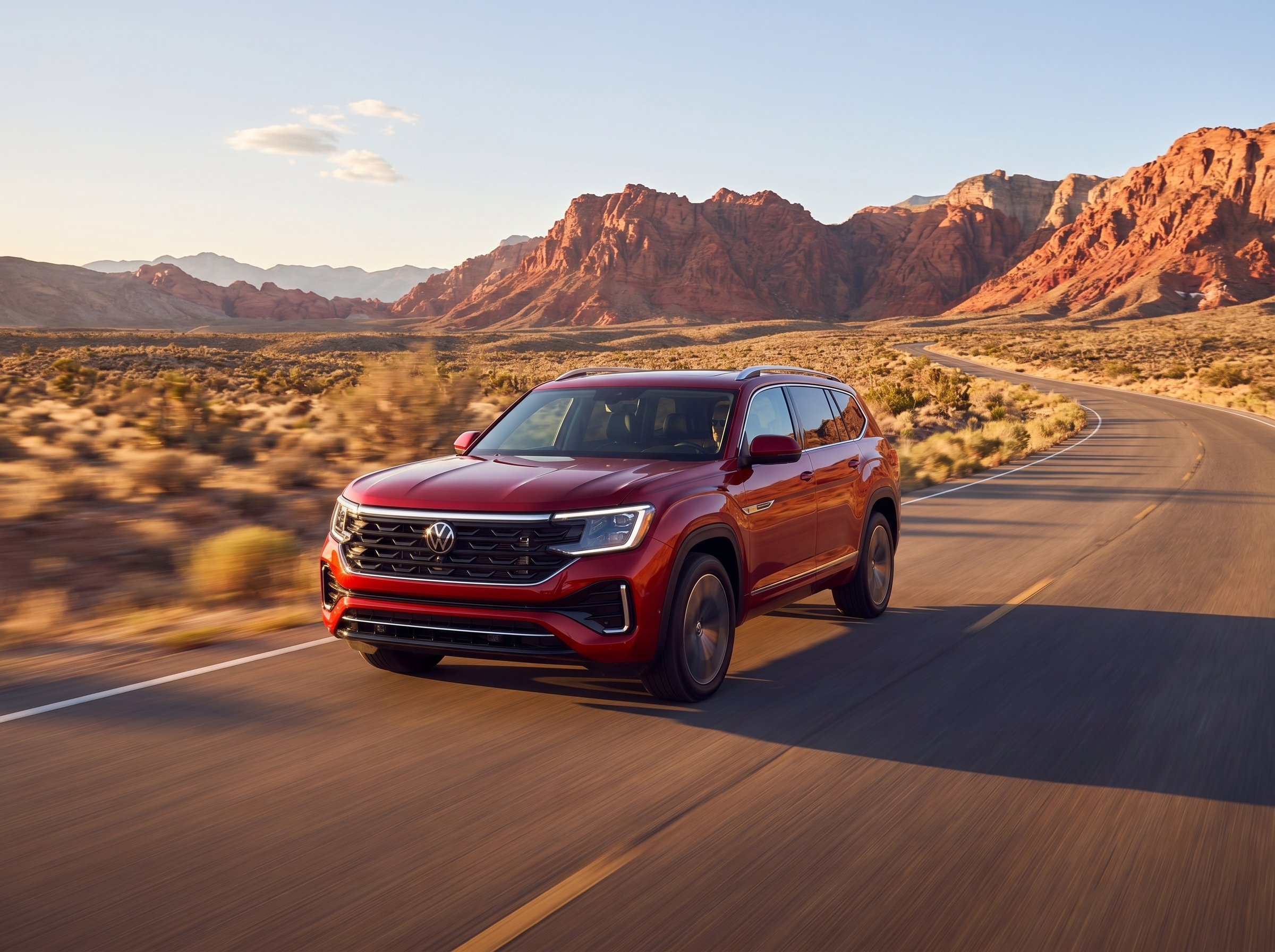 Red Volkswagen Atlas driving on a winding desert road at sunset with red rock formations in the background.