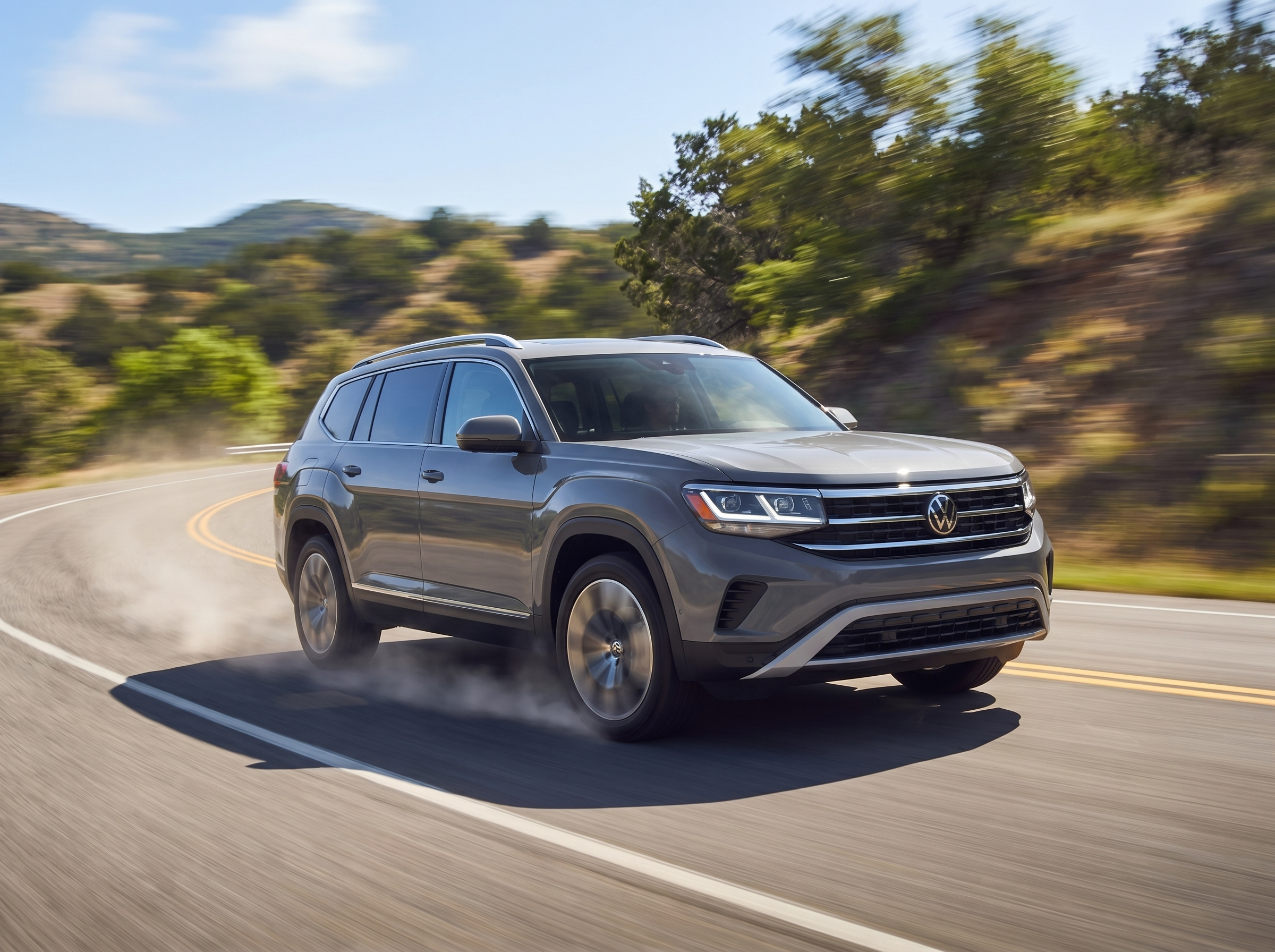 A grey Volkswagen Atlas driving on a winding mountain road with motion blur.