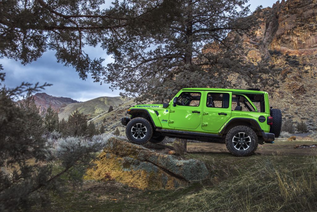 Bright green Jeep Wrangler Rubicon parked with its front tire on a large rock in a mountainous landscape.