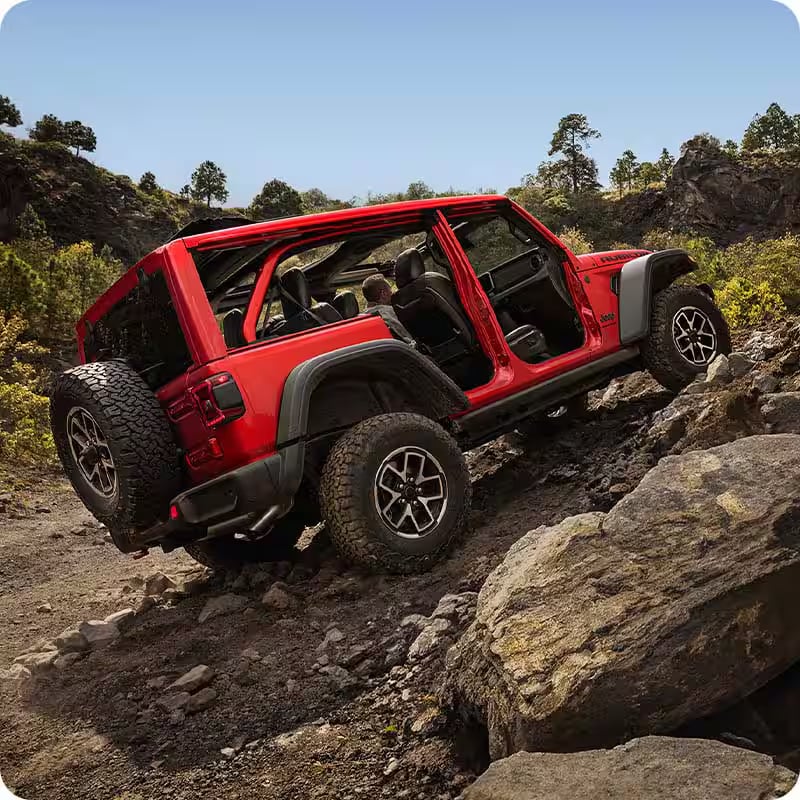 A red Jeep Wrangler Rubicon climbing a rocky, off-road trail with its doors and roof panels removed.