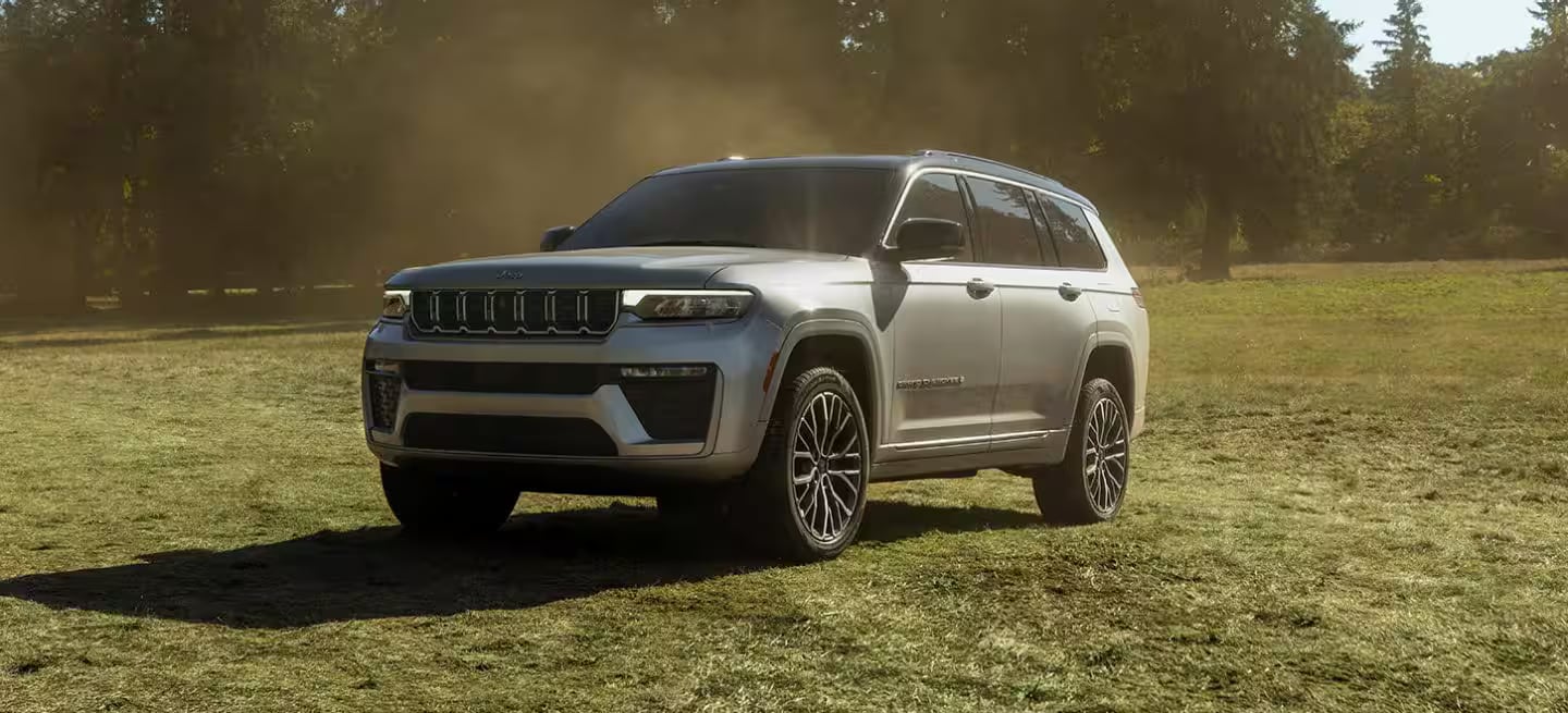 Silver Jeep Grand Cherokee L parked on a grassy field with trees in the background