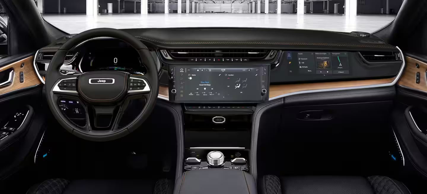 Dashboard and front interior of a modern Jeep SUV, showcasing three digital displays and premium wood trim.