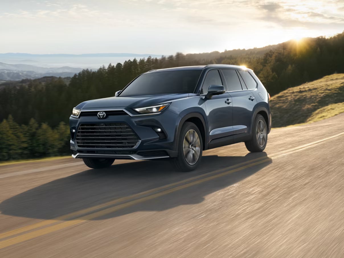 Dark blue Toyota Grand Highlander driving on a winding paved road at sunset.