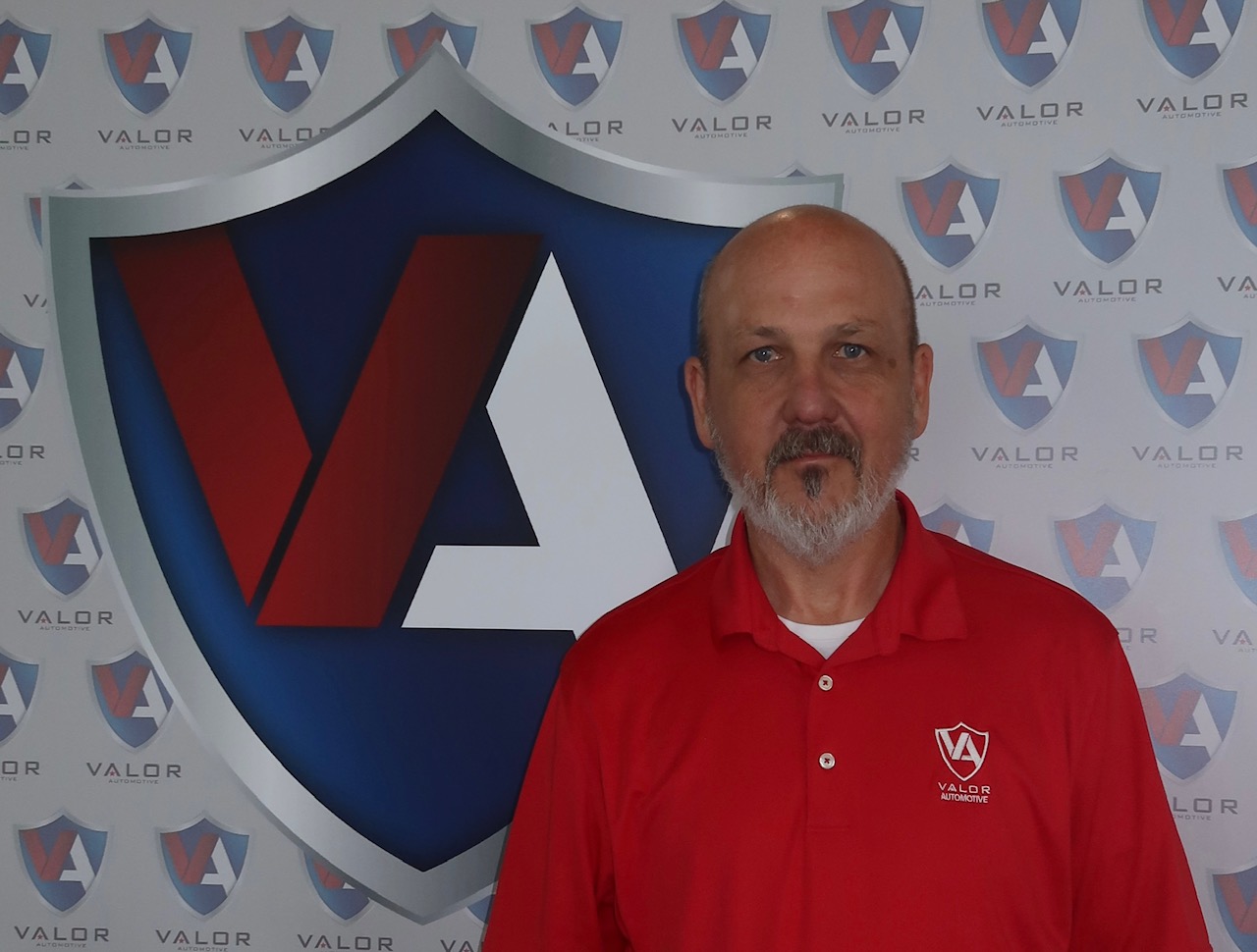 Man with a beard wearing a red Valor Automotive polo shirt standing in front of a company branded backdrop.